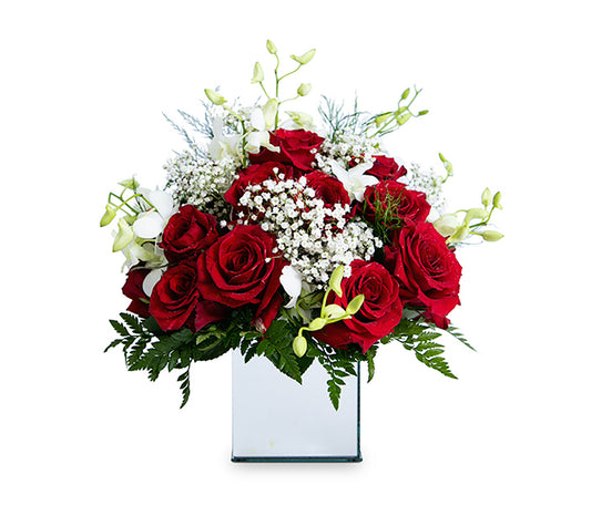 Square mirror vase with 24 red roses, white orchids and baby’s breath.