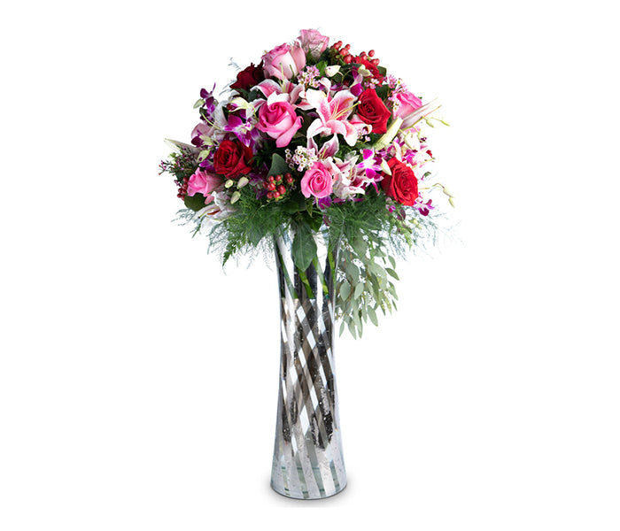 Large vase with red and pink roses, orchids, lilies and cascading greenery.